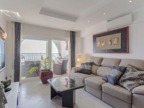A modern living room with a sofa, a coffee table, and a balcony with plants.