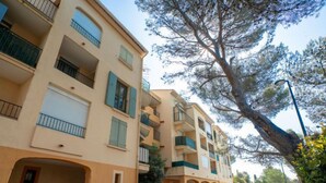 Une rangée d’immeubles résidentiels à plusieurs étages, dotés de balcons, une rue bordée d’arbres et une voiture garée.