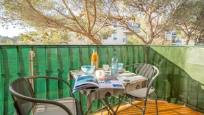 Un balcon avec une table dressée pour deux personnes, des chaises et une barrière en treillis métallique vert.