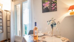Un coin repas avec une table dressée pour deux personnes, une bouteille de vin et un vase rempli de fleurs.