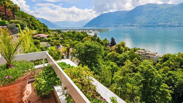 A balcony with potted plants and a view of a lake with mountains in the background. - Lakeview App 501 by Interhome (Ascona)
