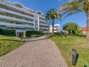 A multi-story hotel with a paved walkway leading to the entrance, surrounded by well-maintained lawns and palm trees. - Riviera Park by Interhome (Cannes)