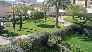 Ein gepflegter Garten mit Palmen, einem ordentlich geschnittenen Heckenstreifen und freiem Blick auf das Meer im Hintergrund.