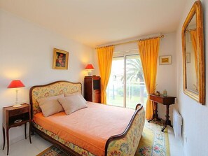 A bedroom with a bed, two bedside lamps, a dresser, a mirror, and a window with curtains. - Riviera Park by Interhome (Cannes)