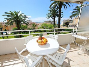 A balcony with a round table and chairs, a fruit bowl, and a view of palm trees and buildings. - Riviera Park by Interhome (Cannes)
