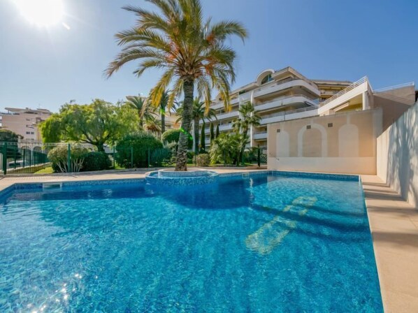 A clear blue swimming pool with a palm tree and a modern building in the background. - Riviera Park by Interhome (Cannes)