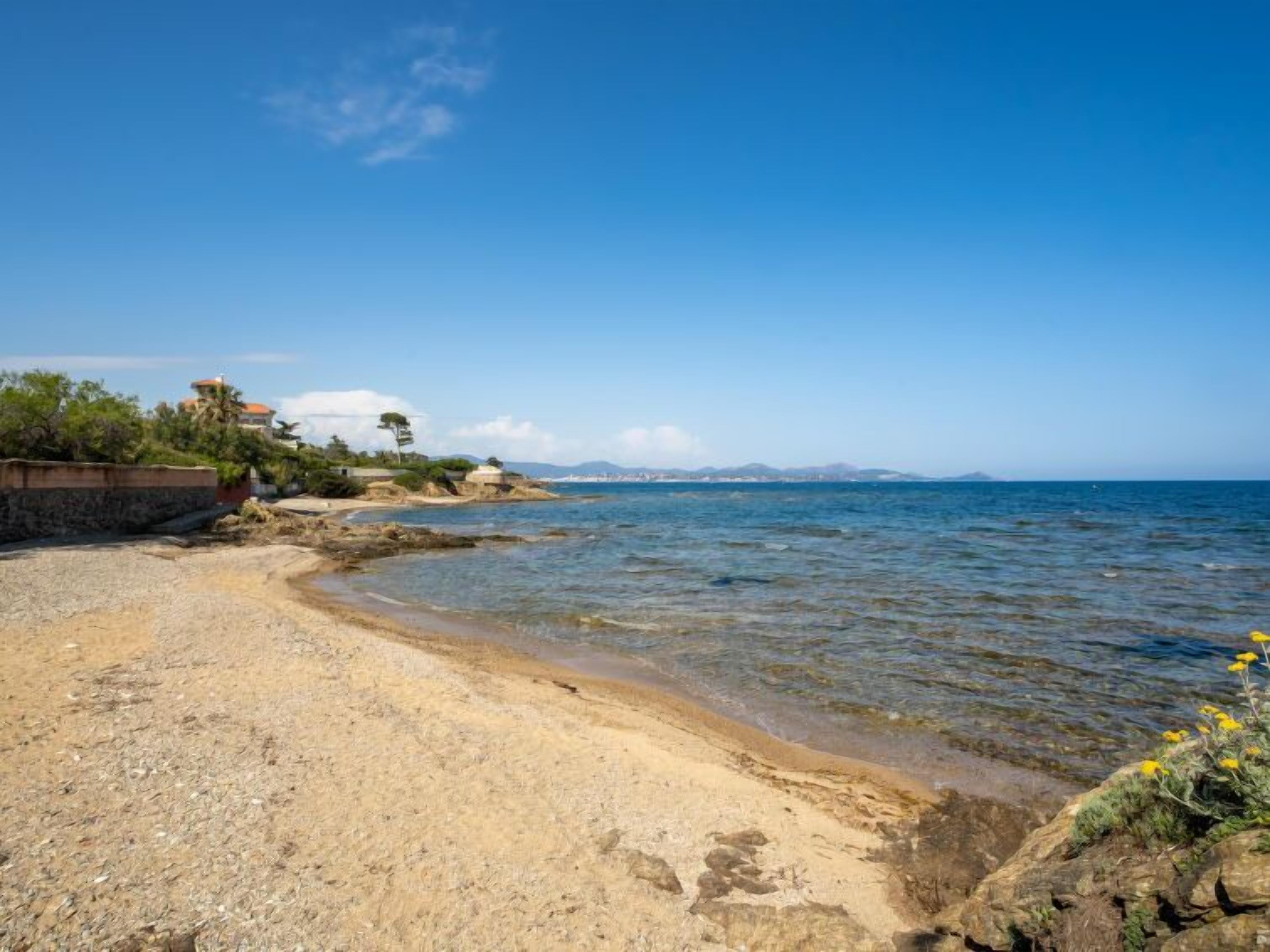 A beach with clear water, a rocky shoreline, and buildings in the background.