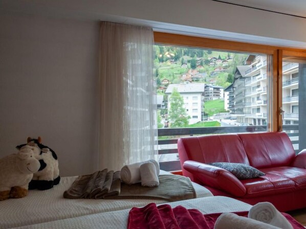 A hotel room with a bed, a red leather sofa, and a view of a mountainous landscape through large windows. - Diana E2 by Interhome (Nendaz)