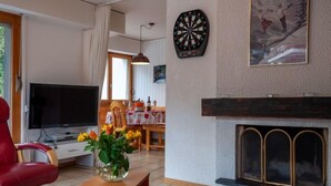 A living room with a television, a fireplace, a dartboard, and a poster on the wall.
