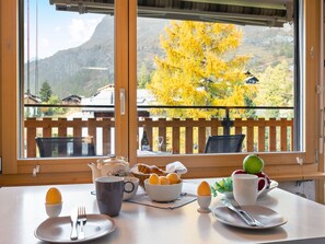 Ein Frühstückstisch mit Eiern, einem Teekessel und Blick auf einen Berg sowie Herbstbäume durch ein Fenster.