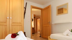 Una habitación de hotel con una cama, una mesita de noche con una toalla blanca enrollada y una rosa roja, un armario de madera y un espejo en la pared.
