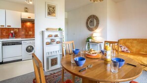 Een moderne keuken met witte kasten, een wasmachine en een eethoek met een houten tafel en stoelen.