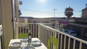 Un balcon avec une table dressée pour le dîner, une bouteille de vin et une vue sur un parking et des immeubles.
