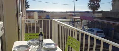 A balcony with a table set for dining, a bottle of wine, and a view of a parking lot and buildings.