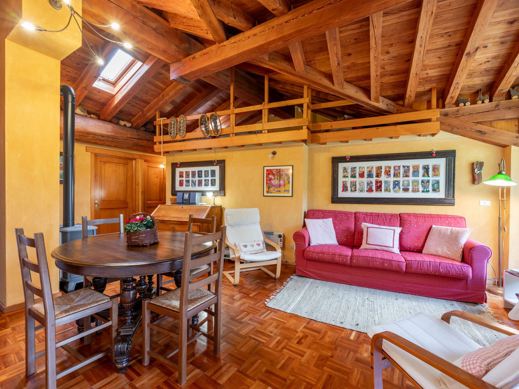 Un intérieur en bois comprenant une table à manger, des chaises, un canapé rouge et un plafond en bois avec des poutres apparentes.