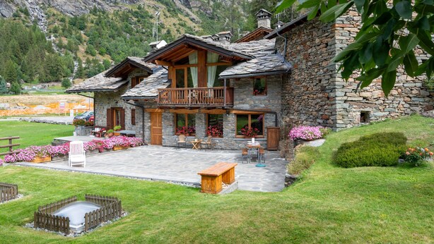 A stone building with a balcony, surrounded by a well-maintained garden and a mountain backdrop. - Chez Les Roset by Interhome (Arvier)