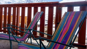 Deux fauteuils de jardin colorés à rayures, avec une clôture en bois et une vue sur les montagnes en arrière-plan.