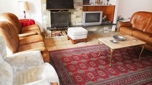 Ein Wohnzimmer mit Ledersofas, einem Kamin, einem Fernseher und einem gemusterten Teppich.