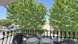 Un área de comedor al aire libre con una mesa preparada para dos personas, rodeada por una barandilla metálica y árboles en el fondo.