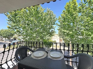An outdoor dining area with a table set for two, surrounded by a metal railing, and trees in the background.