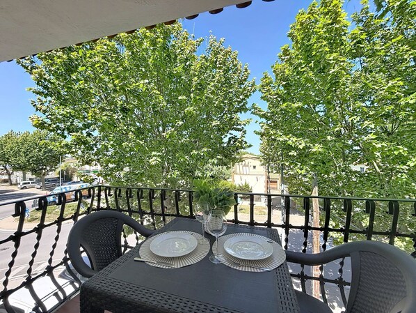Un espace extérieur aménagé pour prendre les repas, avec une table dressée pour deux personnes, entouré d’une rambarde en métal et des arbres en arrière-plan.