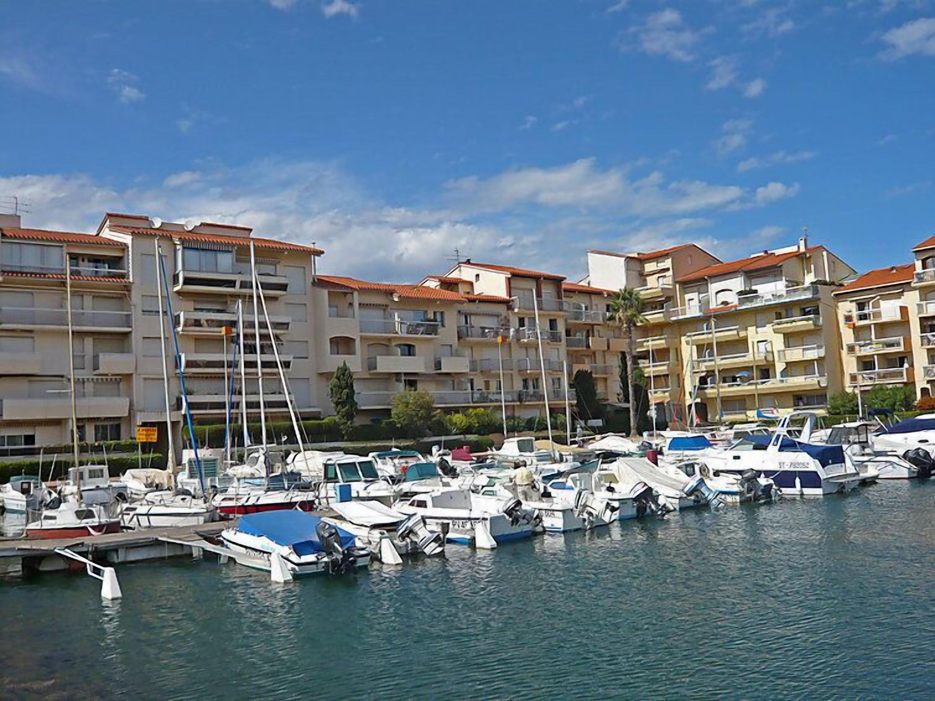 Un puerto deportivo con varias embarcaciones amarradas, rodeado de edificios residenciales de varios pisos con balcones.