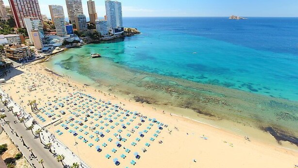 Une plage bordée de rangées de transats et baignée par une mer d’un bleu limpide.