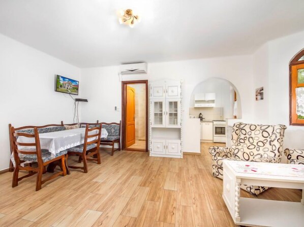 A dining area with a wooden table and chairs, a kitchen with white cabinets, and a patterned sofa. - Vacation home Green by Interhome (Balatonmariafurdo)