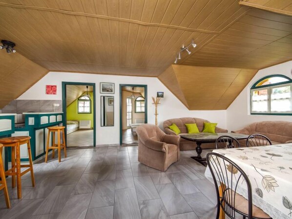 Spazioso loft con soffitto alto, zona pranzo con tavolo e sedie, divano con cuscini e angolo cottura con sgabelli da bar.
