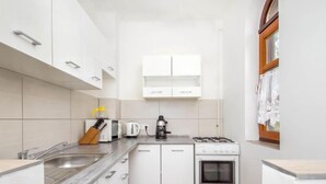 Una cocina compacta con armarios blancos, estufa a gas, cafetera y tostadora.