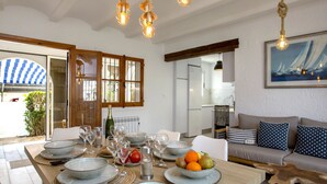 A dining area with a wooden table set for a meal, a kitchen in the background, and a living area with a sofa and cushions. - Pueblo Andaluz by Interhome (Dénia)