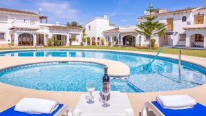 A pool area with lounge chairs and a table, surrounded by white buildings with tiled roofs. - Pueblo Andaluz by Interhome (Dénia)