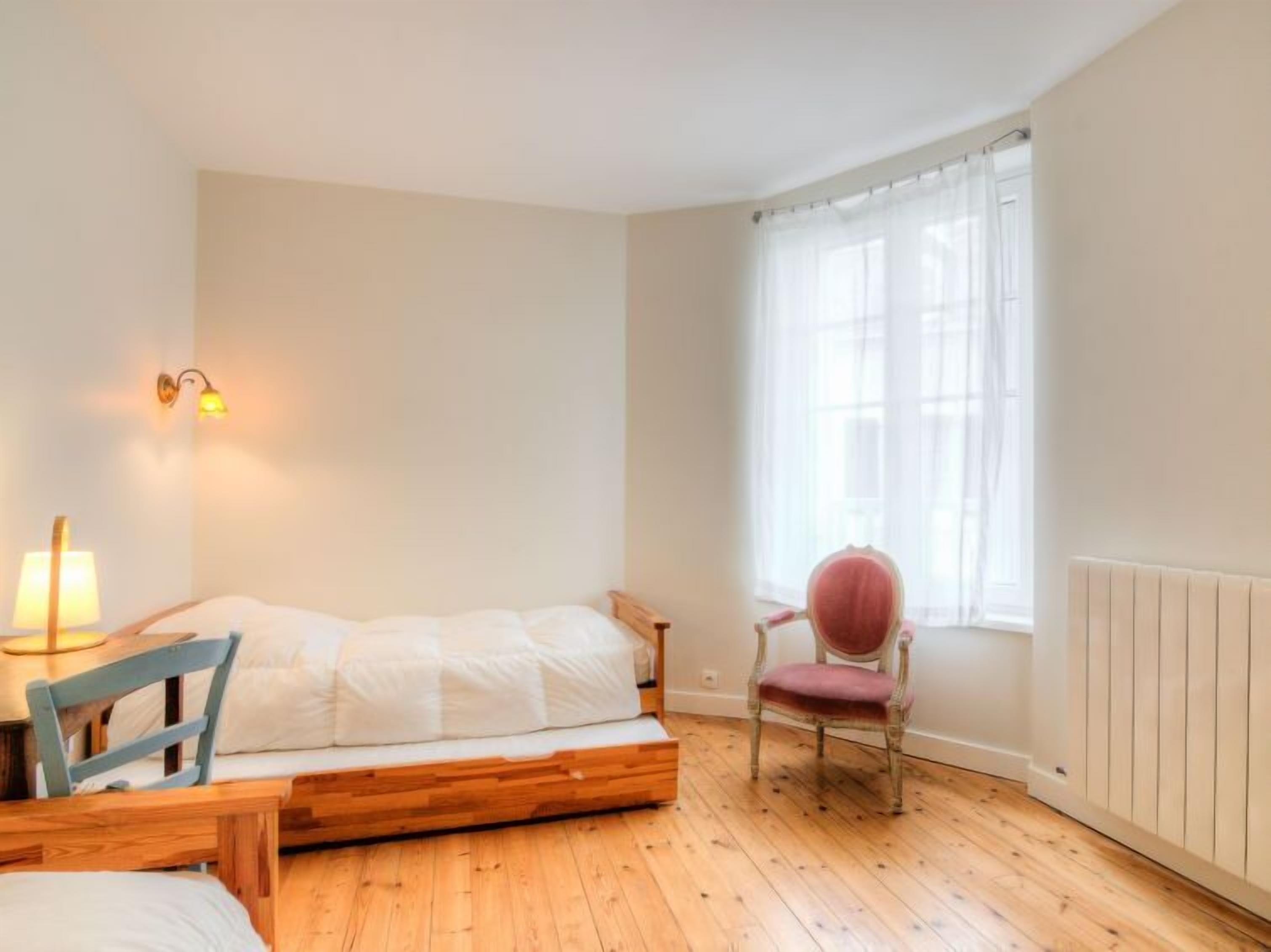 A small, cozy room with a single bed, a chair, a table, and a window with curtains.