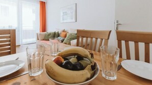 Uma sala de jantar com mesa de madeira posta para dois, uma tigela de fruta e dois copos de água.