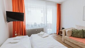 Quarto de hotel com duas camas, um sofá, uma TV e vista para a varanda.