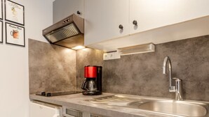 Eine moderne Küche mit Spüle aus Edelstahl, einer roten Kaffeemaschine, einem Backofen und einer Mikrowelle.
