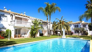 A swimming pool surrounded by white buildings with balconies, palm trees, and a clear blue sky. - La Giralda by Interhome (Dénia)