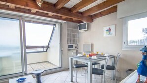 Un coin repas avec une table dressée pour quatre personnes, un téléviseur fixé au mur et une vue sur la mer par une grande fenêtre.