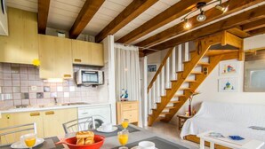 Une cuisine chaleureuse avec un coin repas, un escalier en bois et un lit doté d’une tête de lit blanche.