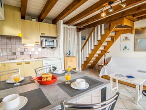 A cozy kitchen with a dining area, wooden staircase, and a bed with a white headboard. - Apartment MEN DU by Interhome (Carnac)