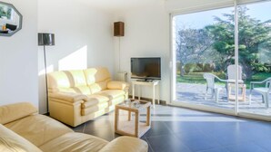 Una sala moderna con un sofá, una mesa de centro, un televisor y un amplio ventanal corredera que da a una zona de estar exterior.