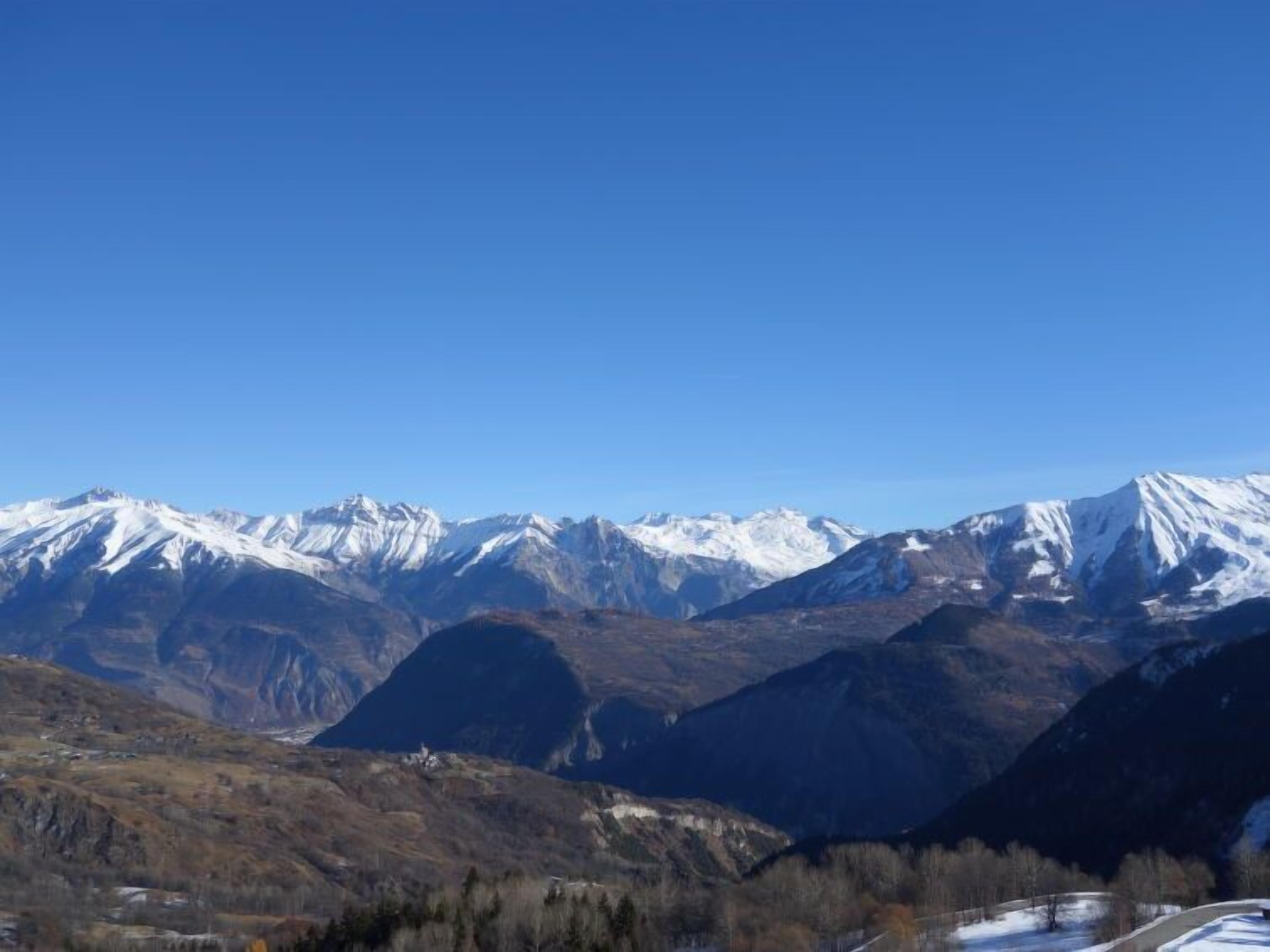 Un paysage montagneux aux sommets enneigés, sous un ciel bleu et dégagé.