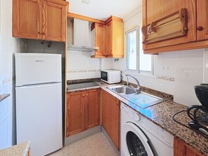 Eine kleine Küche mit Holzausstattung, einem weißen Kühlschrank, einer Mikrowelle, einem Spülbecken und einer Waschmaschine.