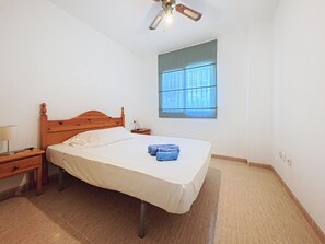 A bedroom with a wooden bed, a nightstand, a lamp, and a window with blinds. - Residencial Daly by Interhome (Dénia)