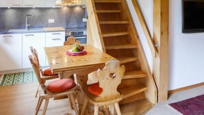 Eine Küche mit einer Holztreppe, einem Esstisch mit Stühlen und einer Pendelleuchte.
