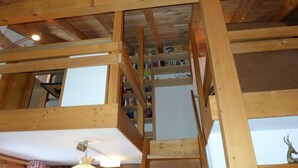 Ein Holzinnenraum mit einer Treppe zu einem Erkerbereich, Bücherregalen und einem kleinen Tisch mit einer Lampe.