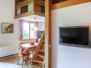 A dining area with a wooden table and chairs, a staircase, a TV mounted on the wall, and a window with curtains. - Chalet Blaugletscher by Interhome (Grindelwald)