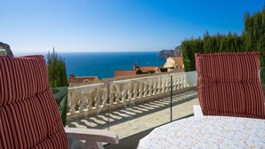 A balcony with two striped chairs and a table, overlooking a coastal view with houses and cliffs. - Pueblo de la Luz by Interhome (Benitachell)