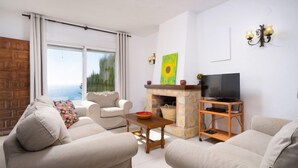 A living room with two sofas, a TV stand, a fireplace, and a large window with a view. - Pueblo de la Luz by Interhome (Benitachell)