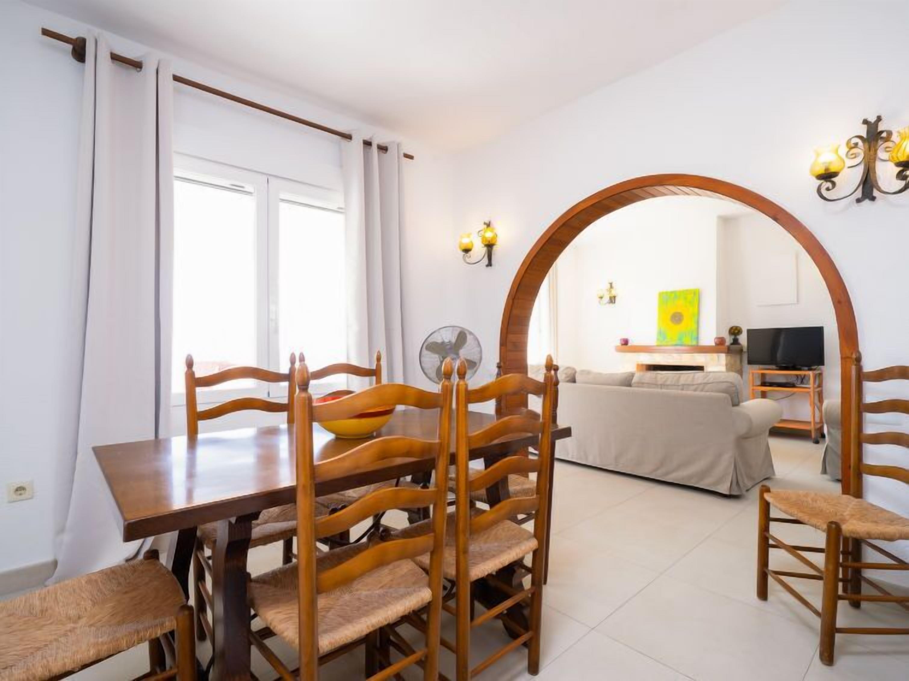 Een eethoek met een houten tafel en stoelen, een ventilator en een bank op de achtergrond.